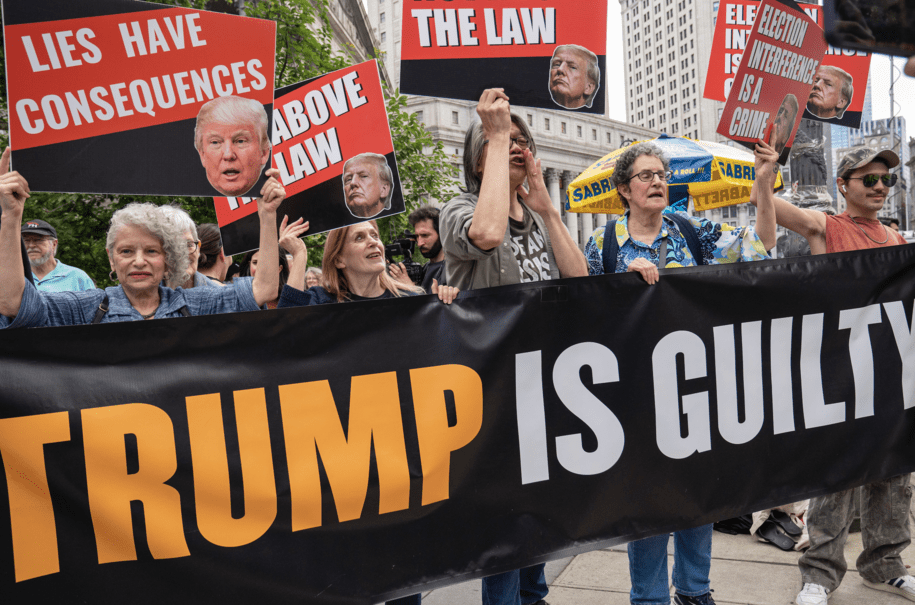 NEW YORK, NEW YORK - MAY 30: People hold signs after former President Donald Trump was found guilty on all counts at Manhattan Criminal Court on May 30, 2024 in New York City. Donald Trump was found guilty on all 34 felony counts of falsifying business records in the first of his criminal cases to go to trial. (Photo by Robert Nickelsberg/Getty Images)