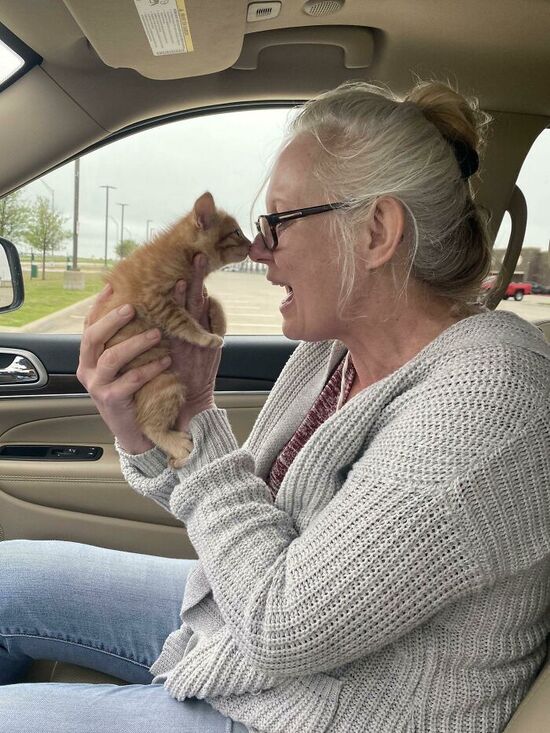 Granny holds a ginger kitten up to touch noses with it,  looking very happy.