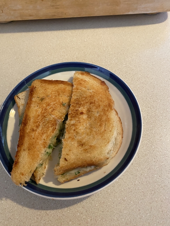 a grilled cheese sandwich cut diagonally with herby cheese oozing out of the center on a white plate with a blue rim