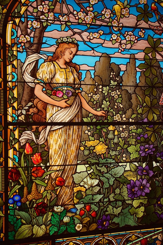 stained glass picture of a woman in pre-Raphaelite gown, among many flowers and trees.